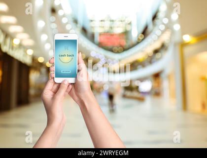 Frau mit Smartphone mit Wort Cashback und Einkaufswagensymbol drinnen, Nahaufnahme. Leerzeichen für Text Stockfoto