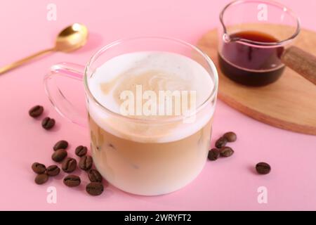 Tasse frischen Kaffee und Bohnen auf rosa Tisch, Nahaufnahme Stockfoto