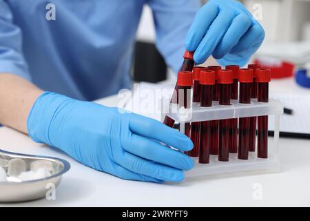 Labortests. Arzt mit Blutproben in Röhrchen am weißen Tisch drinnen, Nahaufnahme Stockfoto