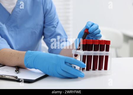 Labortests. Arzt mit Blutproben in Röhrchen am weißen Tisch drinnen, Nahaufnahme Stockfoto