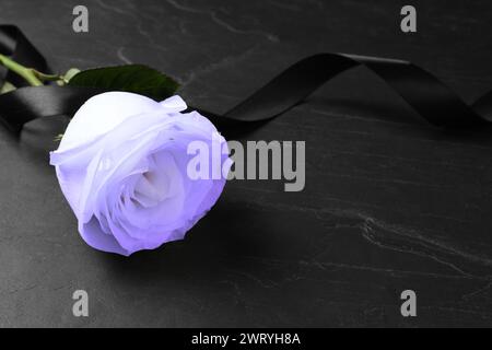 Violette Rose mit schwarzem Trauerband auf dunklem Tisch, Nahaufnahme. Leerzeichen für Text Stockfoto