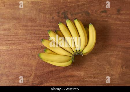 Ein Haufen frischer Bananen auf einem Holztisch, geerntete reife tropische Früchte mit hellgelber Schale und herrlich süßem Geschmack Stockfoto
