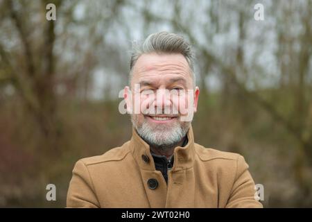 Porträt eines Mannes mittleren Alters mit grauem Haar und grauem Bart im Winter oder Frühling in einem Park Stockfoto