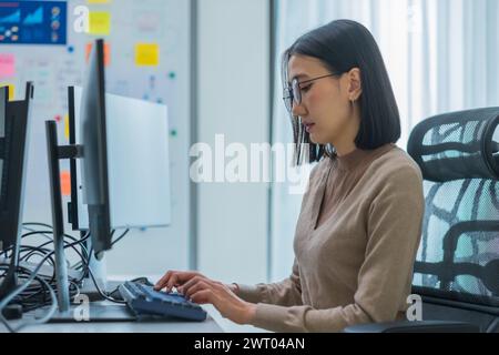 Asiatischer Ingenieur, der die Software-Daten vor dem Computermonitor im Büro codiert Stockfoto