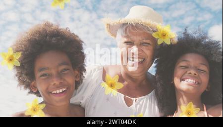 Bild von Blumen über glücklicher afroamerikanerin mit Enkeln am sonnigen Strand Stockfoto
