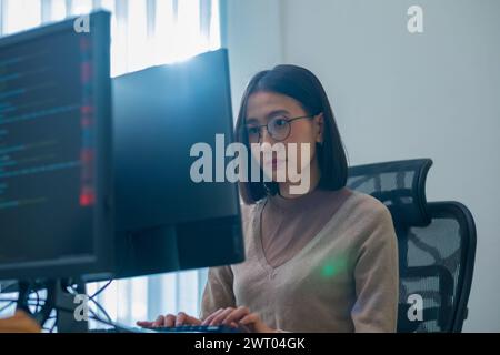 Asiatischer Ingenieur, der die Software-Daten vor dem Computermonitor im Büro codiert Stockfoto