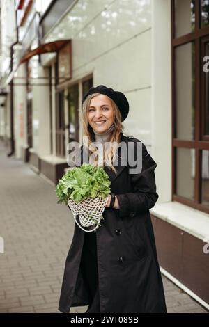 Eine Frau, die steht und einen Haufen Salat vor ihrem Gesicht hält. Vertikales Bild. Stockfoto