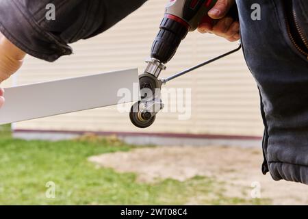 Blechschneidwerke werden von einem elektrischen Bohrer gedreht, der als Adapterbefestigung dient, Dachdecker schneidet Dachstahl im Freien. Stockfoto