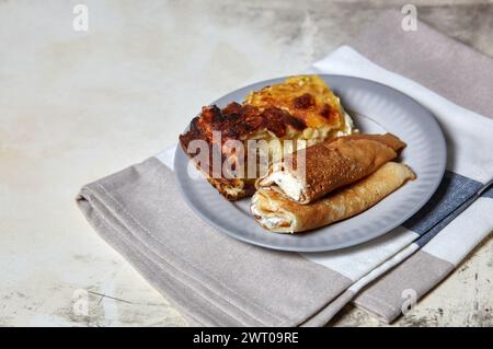 Gerollte Pfannkuchen mit Hüttenkäse und Rosinen und ein Teil Hüttenkäse-Auflauf auf Teller. Ein köstliches süßes Dessert Stockfoto