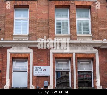 Rotes Backsteingebäude mit Fenstern und einem Schild in der Rupert Street W1 auf Englisch und Chinesisch. Soho, London, England, Vereinigtes Königreich. Stockfoto