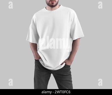 Modell eines weißen übergroßen T-Shirts auf bärtigem Mann mit Händen in Taschen dunkler Jeans, trendiges Hemd, isoliert auf Hintergrund. Männer Streetwear für Design Stockfoto