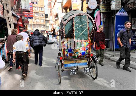 Eine bunt dekorierte Rikscha fährt entlang einer belebten Straße mit Fußgängern, Eindrücke von Nepal, Fahrt vom Pokhara-Tal nach Kathmandu Nepal Stockfoto