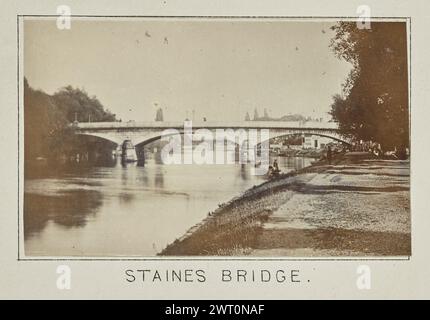 Staines Bridge. Henry W. Taunt, Fotograf (Britisch, 1842 - 1922) 1897 eines von drei Fotos mit Tippeingabe, die eine gedruckte Karte von Laleham, Chertsey und der Umgebung entlang der Themse illustrieren. Das Foto zeigt einen Blick auf die Staines Bridge und einen unbefestigten Fußweg, der parallel zum Fluss verläuft, auf der rechten Seite des Bildes. Zwei Männer schweben in einem Boot in der Nähe des Flusses, gegenüber einem Mann, der auf dem Gras zwischen dem Fluss und dem daneben liegenden Schleppweg steht. (Recto, Mount) unten in der Mitte, unter dem Bild, in schwarzer Tinte gedruckt: „STAINES BRIDGE“. Stockfoto