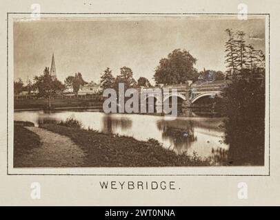 Weybridge. Henry W. Taunt, Fotograf (britischer Fotograf, 1842–1922) um 1886 eines von drei Fotos, die eine gedruckte Karte von Shepperton, Sunbury, Walton-on-Thames und der Umgebung entlang der Themse illustrieren. Das Foto zeigt einen Blick auf die Wey Bridge über den Fluss Wey. Städtische Gebäude säumen das Ufer auf der anderen Seite des Flusses, einschließlich der Kirche St. James, dessen Turm durch die Bäume zu sehen ist. (Recto, Mount) unten in der Mitte, unter dem Bild, in schwarzer Tinte gedruckt: „WEYBRIDGE“. Stockfoto