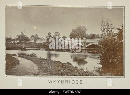 Weybridge. Henry W. Taunt, Fotograf (Britisch, 1842 - 1922) 1897 eines von drei Fotos mit Tippkarten, die eine gedruckte Karte von Shepperton, Sunbury, Walton-on-Thames und der Umgebung entlang der Themse illustrieren. Das Foto zeigt einen Blick auf die Wey Bridge über den Fluss Wey. Städtische Gebäude säumen das Ufer auf der anderen Seite des Flusses, einschließlich der Kirche St. James, dessen Turm durch die Bäume zu sehen ist. (Recto, Mount) unten in der Mitte, unter dem Bild, in schwarzer Tinte gedruckt: „WEYBRIDGE“. Stockfoto