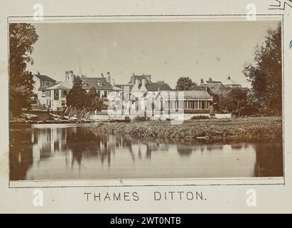 Thames Ditton. Henry W. Taunt, Fotograf (Britisch, 1842 - 1922) 1897 eines von drei Fotos mit Tippeingabe, die eine gedruckte Karte von Kingston und der Umgebung, einschließlich Hampton Court Park und Bushy Park, entlang der Themse, illustrieren. Das Foto zeigt einen Blick auf das Swan Hotel am Flussufer in Thames Ditton von der anderen Seite des Wassers. An der Bootsanlegestelle des Hotels befinden sich mehrere Boote, die an den Docks befestigt sind, und zwei Männer stehen oben auf der Treppe, die zum Wasser führt. (Recto, Mount) unten in der Mitte, unter dem Bild, in schwarzer Tinte gedruckt: „THAMES DITTON“. Stockfoto