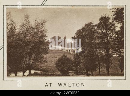 In Walton. Henry W. Taunt, Fotograf (britischer Fotograf, 1842–1922) um 1886 eines von drei Fotos, die eine gedruckte Karte von Shepperton, Sunbury, Walton-on-Thames und der Umgebung entlang der Themse illustrieren. Das Foto zeigt einen Blick auf die Walton Bridge durch Bäume, die am Flussufer wachsen. (Recto, Mount), unten in der Mitte, unter dem Bild, in schwarzer Tinte gedruckt: „AT WALTON“. Stockfoto