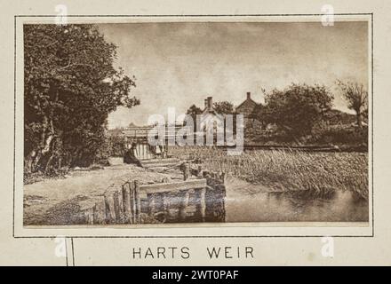 Harts Weir. Henry W. Taunt, Fotograf (britischer Fotograf, 1842–1922) um 1886 eines von drei Fotos, die eine gedruckte Karte von Kelmscott, Thrupp und der Umgebung entlang der Themse illustrieren. Das Foto zeigt einen Blick auf Harts Weir am Fluss nahe Appleton. Ein Mann sitzt mit seinen Beinen über der Seite der hölzernen Stützkonstruktion am linken Ufer, und eine hölzerne Fußgängerbrücke überquert den Fluss im Hintergrund und führt zu mehreren Steinbauten. (Recto, Halterung) unten in der Mitte, unter dem Bild, in schwarzer Tinte gedruckt: „HARTS WEIR“ Stockfoto