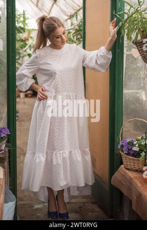 Eine junge Frau in weißem Kleid in einem Glasgewächshaus Stockfoto