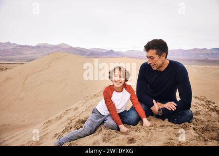 Glücklicher Sohn, der mit Vater auf der Sanddüne im Death Valley sitzt Stockfoto