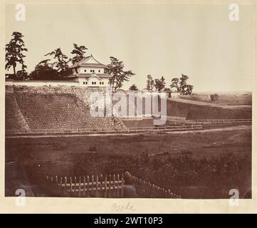 Osaka. Unbekannt, Fotograf aus den 1850er–1890er Jahren Blick auf das Gelände der Burg Osaka aus der Nähe des äußeren Grabens. Der Sengan-Yagura-Turm befindet sich in der hohen Steinmauer, die die Burg neben dem Otemon-Tor umgibt. Der äußere Graben umgibt die Steinmauer und die Brücke, die zum Tor führt. Ein hölzerner Zaun säumt die Nähe des Grabens, und ein kleinerer hölzerner Pfahlzaun umgibt ein Stück Land im Vordergrund. (Recto, Mount) untere Mitte, handgeschrieben in Bleistift: 'Osaka' Stockfoto