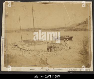 Der "Morgenstern" in Anchor. Unbekannt, Fotograf ca. 1880–1895 Ein Schiff legte in einem Hafen an, der mit Steinen gesäumt war. Das Schiff hat zwei Masten ohne Segel und ist mit mehreren Planken am Ufer gesichert. Zwei Figuren stehen neben dem Boot und zwei Jungen sitzen im Vordergrund auf dem Boden. Ein weiteres Boot befindet sich etwas vor der Küste im Hintergrund. (Recto, Mount) Mitte links, Bleistift: „3“; (Recto, Mount) unten Mitte, Bleistift: '4'; Stockfoto