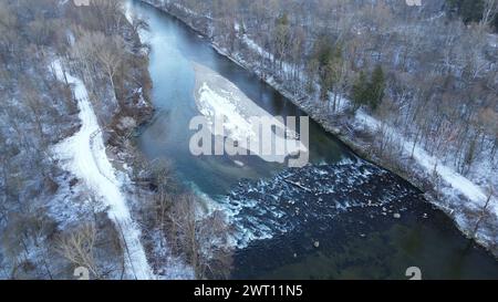 Die sanfte Umarmung des Winters auf einem ruhigen Fluss, flankiert von schneebedeckten Bäumen Stockfoto