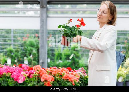 Junge Erwachsene freudige Frau, die bunte Topfblumen auf dem Gartenmarkt wählt. Frühjahrsverkauf blühender Pflanzen in Töpfen bei Botanical Stockfoto