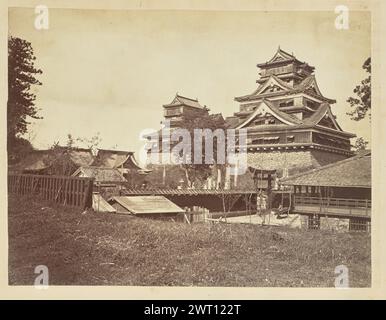 Schloss Kumamoto. Uchida Kuichi, Fotografin aus den 1850er–1890er Jahren Blick auf das Schloss Kumamoto von einem grasbewachsenen Rasen neben dem Komplex. Das Hauptgebäude der Burg steht auf einer Steinmauer und überragt die übrigen Gebäude um sie herum. Ein Mann steht vor dem Torii-Tor in der Randmauer. Stockfoto