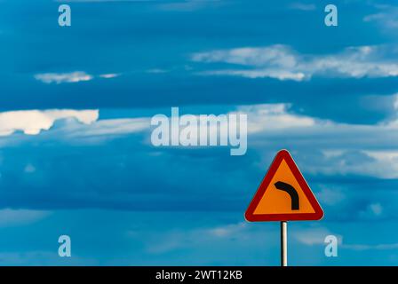 Ein rot-gelbes Straßenschild, das eine scharfe Abbiegung nach links anzeigt, befindet sich am Straßenrand in Schweden. Stockfoto
