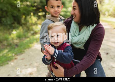 Ein glücklicher Junge klatscht, während die lächelnde Mutter ihre Kleinkinder hält Stockfoto