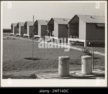 Wohnungen für wandernde Gemüsepflücker, Osceola Labor Camps, gebaut von FSA, Belle Glade, Florida. Marion Post Wolcott, Fotograf (amerikanisch, 1910–1990) 1941 Eine Reihe von Hütten, die für Landarbeiter gebaut wurden, steht neben einem Weg und Rasen. Im Vordergrund befinden sich zwei Papierkorb. (Rückseite, Druck) oben links, in Bleistift: ''77 / MW 157V / Wohnraum für wandernde Gemüsepflücker, / Osceola Arbeitslager, gebaut von FSA, Bella Glade, / Fla. 1941'; Zentrum, in Bleistift: '57247D'; unten links, in Bleistift: 'MPW PG8530'; Stockfoto