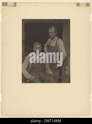 Zwei Männer in Overalls in der Tür einer Scheune. Doris Ulmann, Fotograf (Amerikaner, 1882–1934) 1925–1934 Porträt zweier Männer im Gesamtbild, in der Tür einer Scheune. Der Mann auf der linken Seite sitzt in frontaler Position. Er trägt eine Brille und hält einen Hammer in der rechten Hand und einen Meißel in der linken Hand. Der Mann rechts ist jünger. Er steht im Dreiviertelwinkel, seine Hände auf den Hüften. (Rückseitig, Halterung) oben links, mit rotem Bleistift: '242-A[seitlich]'; Stockfoto
