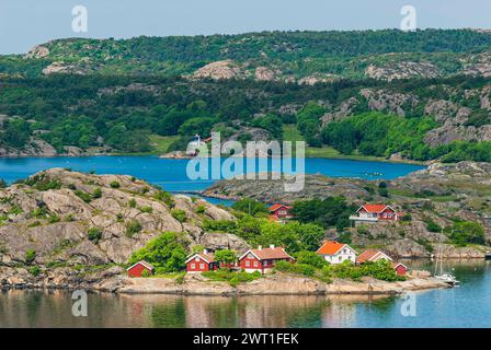 In Bohuslän, Schweden, sonnt sich ein ruhiges Küstendorf unter der Sommersonne. Rote und weiße traditionelle Häuser säumen die zerklüftete Küste, umgeben von c Stockfoto