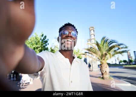 Fröhlicher afrikanischer junger Mann, der ein Selfie macht und die Kamera lächelnd ansieht, soziale Medien teilt. Stockfoto