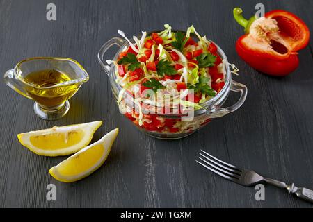 Vegetarischer Gemüsesalat aus gehacktem Kohl und Paprika, gekleidet mit Olivenöl und Zitrone in einer Glasschale auf einem schwarzen Holztisch Stockfoto