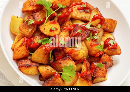 Knusprig gebratene Patata Bravas, gebratene spanische Kartoffeln mit geräucherter Paprika-Sauce in weißer Schüssel, Nahaufnahme Stockfoto