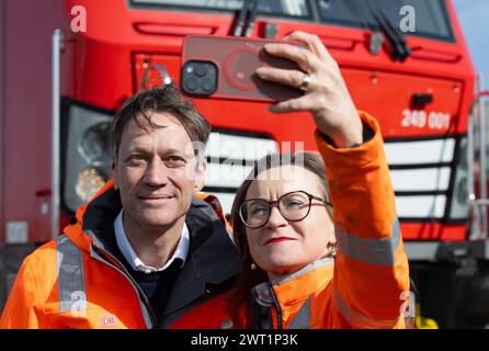 15. März 2024, Sachsen-Anhalt, Halle (Saale): Sigrid Nikutta, CEO von DB Cargo, macht ein Selfie mit Michael Peter, Geschäftsführer von Siemens Mobility, vor einer neuen Hybridlokomotive im Güterbahnhof. Künftig wird die neue Generation von Lokomotiven rein elektrisch auf elektrifizierten Gleisabschnitten fahren, während auf Abschnitten ohne Freileitungen ohne Wechsel der Lokomotiven auf konventionellen Antrieb umgeschaltet werden kann. Die Hybridlokomotiven, die Vectron Dual Mode Light genannt werden, werden vom Bahnanbieter Siemens Mobility hergestellt. Wenn die Lokomotive von Green el angetrieben wird Stockfoto