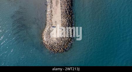 Aus der Vogelperspektive auf einen Wellenbrecher, der sich bis ins Meer erstreckt. Die Ruhe der Meereswellen trifft auf die Struktur. Ideal für Hintergründe oder Reisekonzepte. Kopieren Stockfoto