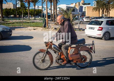 Ein älterer Mann fährt einen Motorroller neben der Großen Moschee in der Medina in Mahdia, Tunesien. Stockfoto