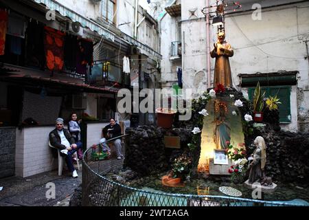 Ein unverwechselbarer Blick auf eine Gasse im Stadtteil Forcella von Neapel. Eine Statue des heiligen Padre Pio vor den Häusern und den Räumlichkeiten, wo viele Stockfoto