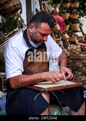 Ein Mann fotografierte, als er den Strohhalm eines Stuhls reparierte Stockfoto