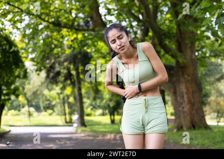 Indische junge Frau, die Sport macht, ihre Hände nach dem Joggen an der Seite ihres Körpers hält, starke Schmerzen spürt, Ruhe braucht. Stockfoto