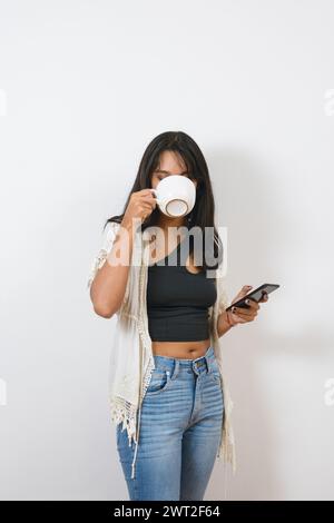 Vertikales Porträt für soziale Medien von jungen lateinfrauen in lässiger Kleidung, schwarzem Haar und Brünette, die zu Hause Kaffee trinken und das Telefon benutzen, Stockfoto
