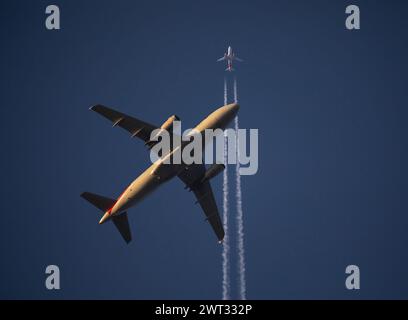 Ein Verkehrsflugzeug in niedriger Höhe passiert kurz nach dem Start bei Sonnenuntergang unter einem Höhenflugzeug. Stockfoto