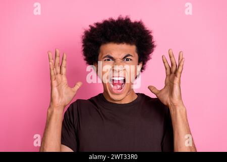 Foto des wütenden jungen lustigen Mannes Arme oben tragen braunes T-Shirt Konflikt Emotionen aggressive Grimasse isoliert auf rosa Hintergrund Stockfoto