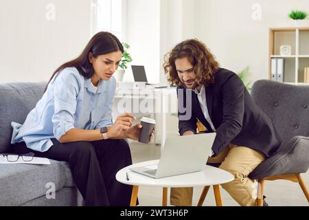 Junge Geschäftsleute, Mann und Frau, die auf Sofa mit Laptop sitzen, während sie sich treffen und unterhalten. Stockfoto
