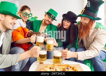 Glückliche Freunde in Kostümen trinken Bier, essen Pizza und haben Spaß am St. Patrick's Day Stockfoto