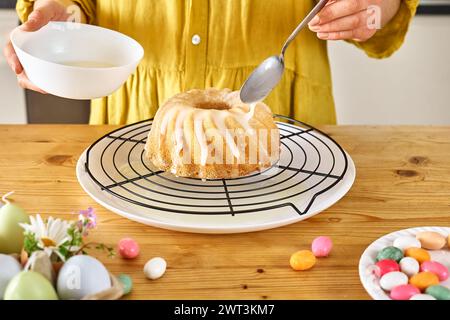 Weibliche Hände, die Glasur auf den Osterkuchen gießen. Traditioneller osterkuchen oder süßes Brot mit Belag. Ostervergnügen. Stockfoto