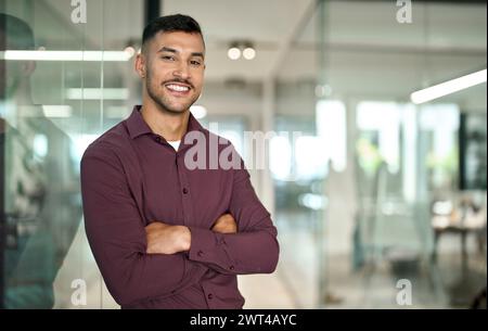 Selbstbewusster junger lateinischer Geschäftsmann, der im Büro die Arme überkreuzt hat, Porträt. Stockfoto